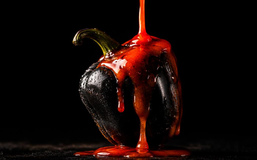 Molho vermelho escorrendo sobre uma pimenta preta em fundo escuro